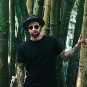 Cool fashion portrait of a man in sunglasses and hat among bamboo trees.