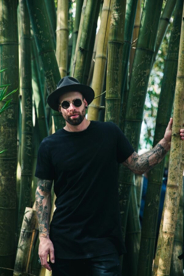 Cool fashion portrait of a man in sunglasses and hat among bamboo trees.