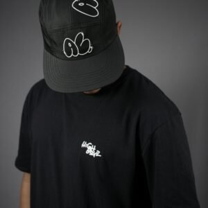 Minimalist fashion portrait of a man wearing a black cap and t-shirt in studio setting.