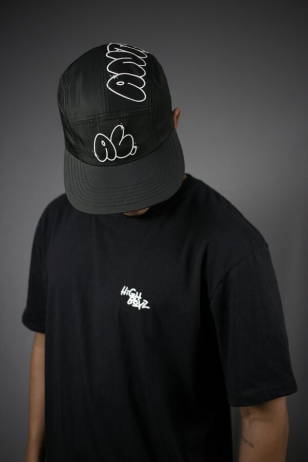 Minimalist fashion portrait of a man wearing a black cap and t-shirt in studio setting.