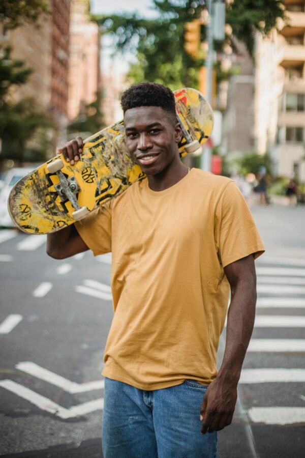 Smiling young man holding skateboard in a city street, capturing energetic urban lifestyle.