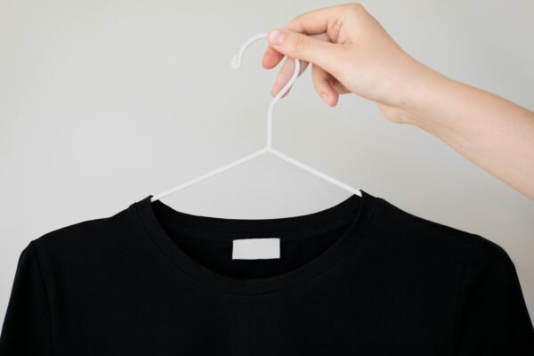 Black t-shirt on hanger with hand holding, perfect for apparel mockups.